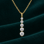 Amara Pendant Necklace: gold-tone drop pendant with five graduated round moissanite stones on teal velvet