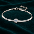Elara Chain Bracelet: slim sterling silver herringbone chain bracelet with a single moissanite centre stone on teal velvet