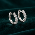 Genevieve Hoop Earrings: sterling silver huggie hoops with a row of claw-set round moissanite stones on teal velvet