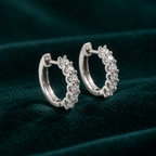Genevieve Hoop Earrings: sterling silver huggie hoops with a row of claw-set round moissanite stones on teal velvet