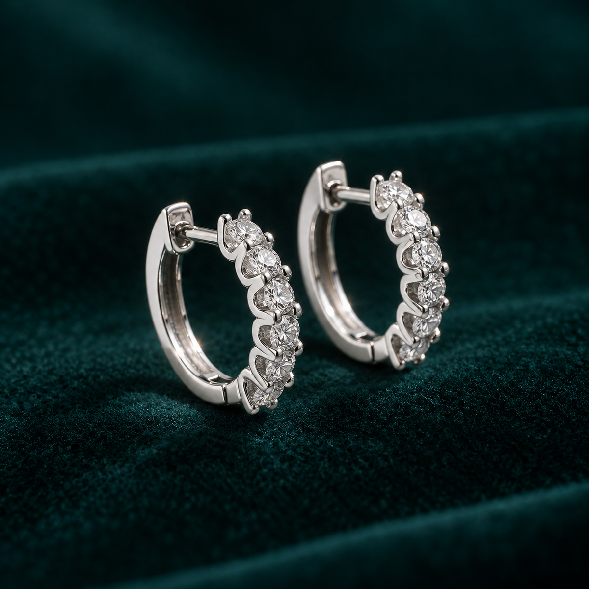 Genevieve Hoop Earrings: sterling silver huggie hoops with a row of claw-set round moissanite stones on teal velvet